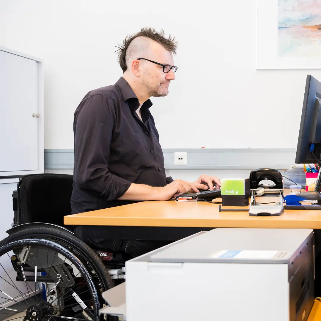 Bürosituation:  Herr Freels sitzt am Schreibtisch und schreibt am Computer. Er trägt ein schwarzes Hemd.